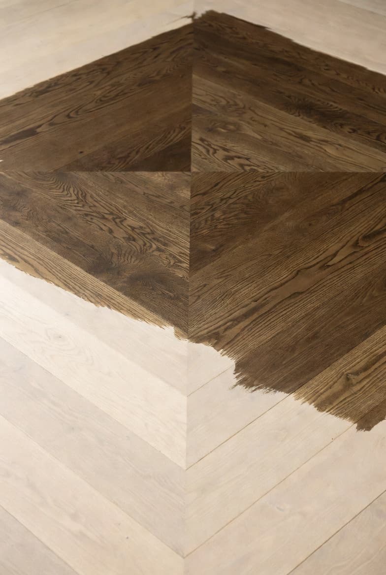 Chevron-pattern hardwood floor with dark stain applied in the center and lighter sanded wood around it.